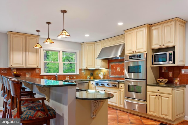 902 Emerald Dr, Alexandria, VA 22308 - kitchen featuring a warming drawer, appliances with stainless steel finishes, wall chimney exhaust hood, cream cabinetry, and a kitchen bar