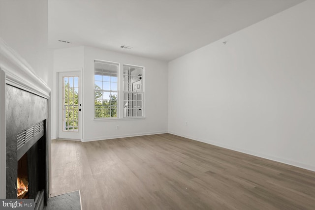 unfurnished living room with wood finished floors, a warm lit fireplace, and baseboards