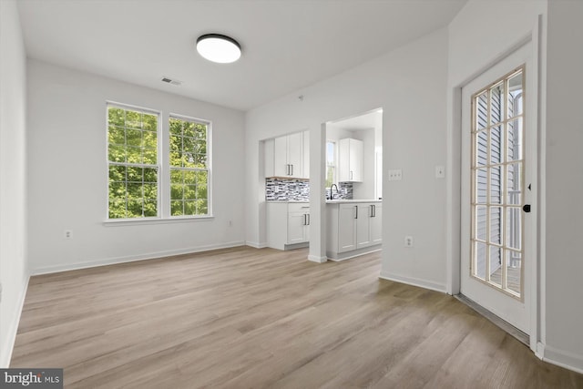 unfurnished living room with light wood-style flooring, baseboards, and a sink