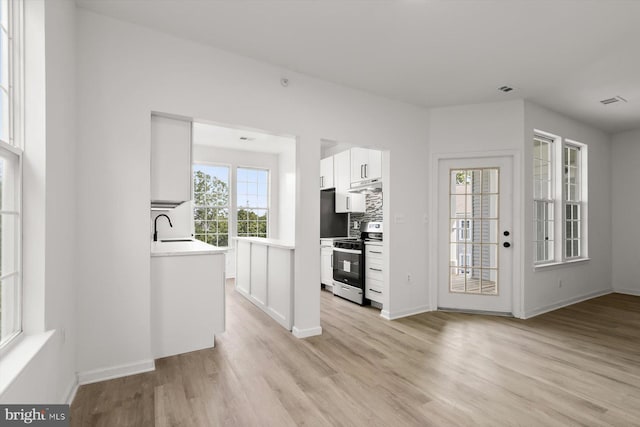 kitchen with electric range, under cabinet range hood, light wood finished floors, a sink, and white cabinets