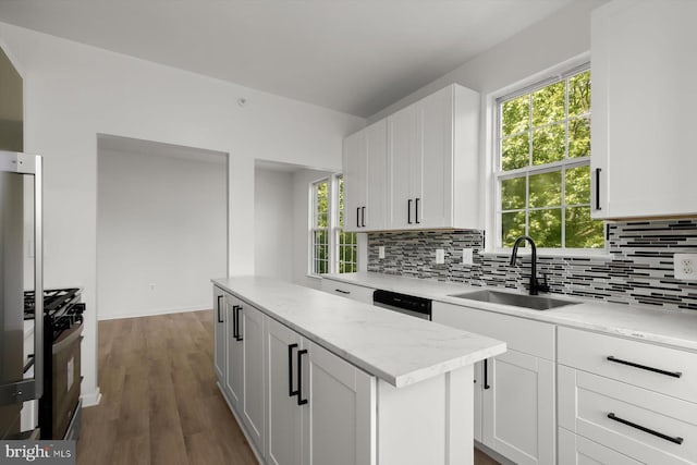 kitchen featuring a sink, gas stove, decorative backsplash, a kitchen island, and white cabinetry
