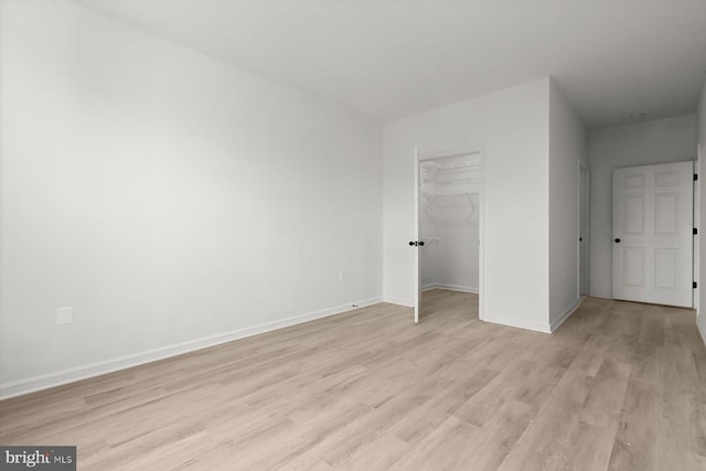 unfurnished bedroom featuring light wood-type flooring, baseboards, a closet, and a spacious closet