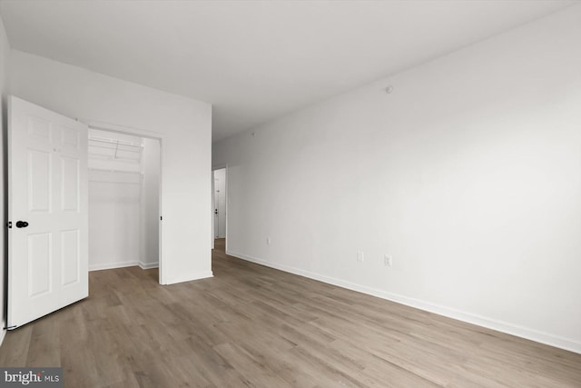 unfurnished bedroom with wood finished floors, attic access, a closet, and baseboards