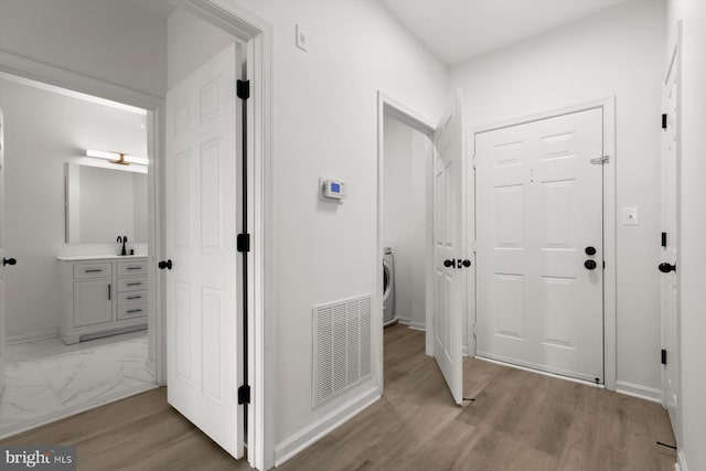 hallway featuring light wood-style flooring, a sink, baseboards, and washer / clothes dryer