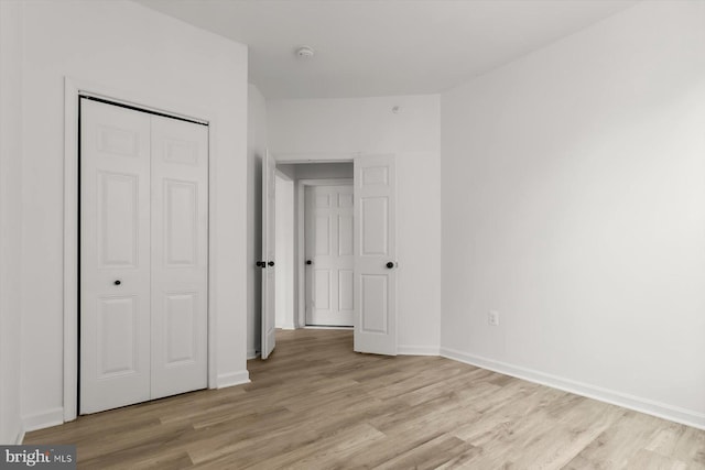 unfurnished bedroom featuring light wood-type flooring, a closet, and baseboards