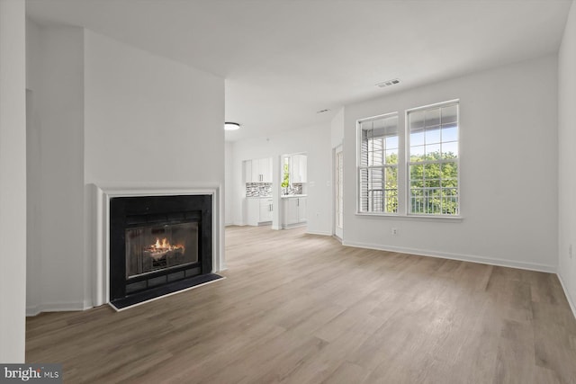 unfurnished living room with wood finished floors, a fireplace with flush hearth, and baseboards