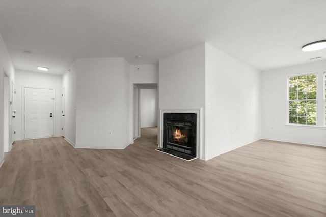unfurnished living room featuring wood finished floors, a warm lit fireplace, and baseboards