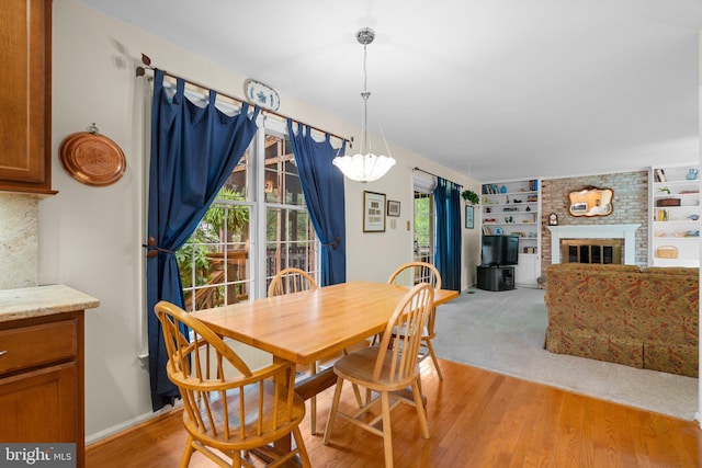 dining room featuring a brick fireplace, a chandelier, and light wood finished floors