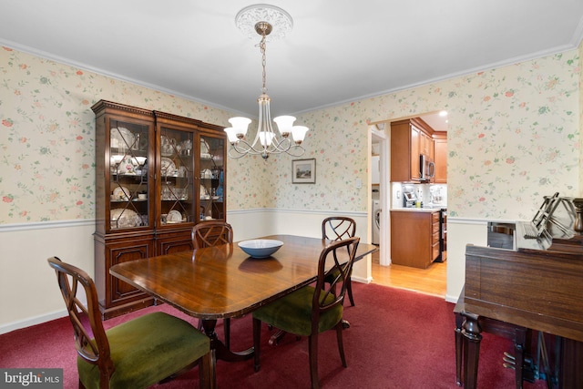 carpeted dining room featuring a wainscoted wall, a chandelier, ornamental molding, wallpapered walls, and washer / dryer
