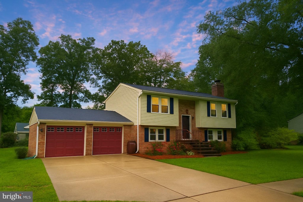 bi-level home featuring an attached garage, driveway, brick siding, a front lawn, and a chimney