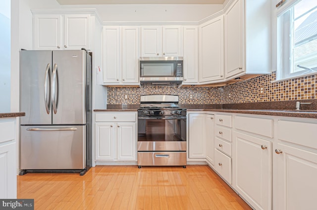 kitchen with appliances with stainless steel finishes, white cabinetry, light wood-style floors, and backsplash