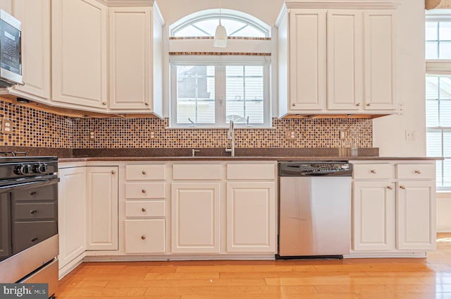 kitchen featuring appliances with stainless steel finishes, a sink, dark countertops, light wood-style flooring, and white cabinets