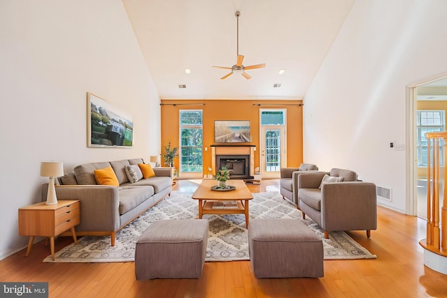 living area featuring hardwood / wood-style floors, healthy amount of natural light, a ceiling fan, a glass covered fireplace, and high vaulted ceiling