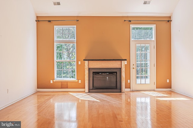 unfurnished living room with hardwood / wood-style flooring, healthy amount of natural light, and a glass covered fireplace