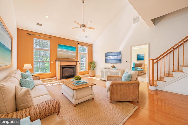 living area featuring plenty of natural light, a ceiling fan, light wood-style flooring, high vaulted ceiling, and a glass covered fireplace