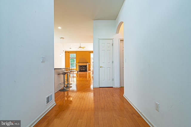 hall with baseboards, light wood-style flooring, arched walkways, and recessed lighting