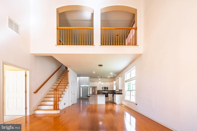 unfurnished living room with light wood finished floors, a towering ceiling, and stairs