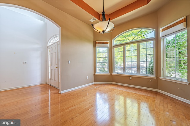 unfurnished room featuring arched walkways, light wood-style flooring, baseboards, and a raised ceiling