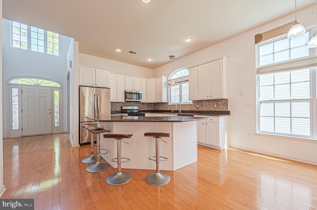 kitchen with appliances with stainless steel finishes, dark countertops, a kitchen breakfast bar, a sink, and light wood finished floors
