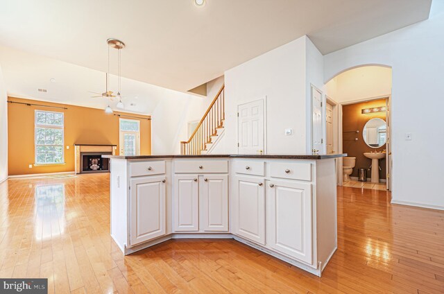 kitchen with light wood-style flooring, dark countertops, white cabinets, and arched walkways