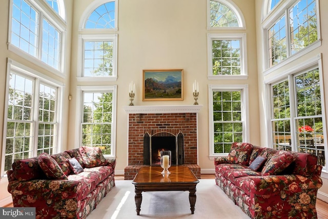 living room with a high ceiling, wood finished floors, and a brick fireplace