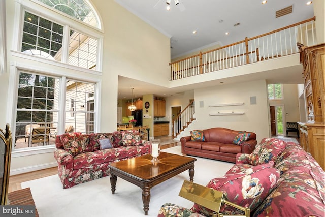 living area with a towering ceiling, healthy amount of natural light, stairs, and wood finished floors