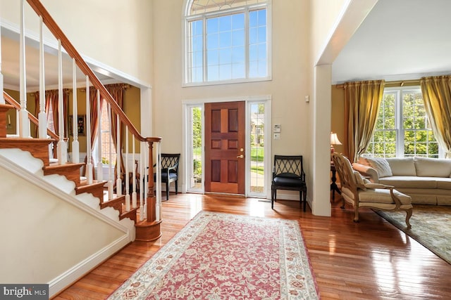 foyer entrance featuring light wood-type flooring, stairway, and a towering ceiling