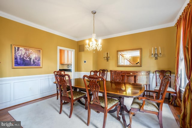 dining room with a chandelier, crown molding, wood finished floors, and wainscoting