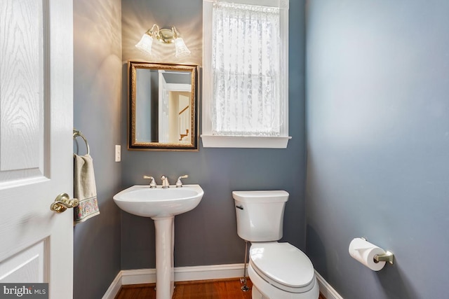 half bath with baseboards, toilet, wood finished floors, and a sink