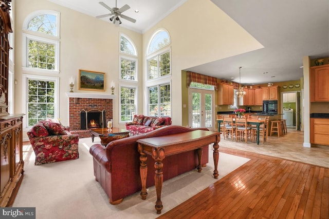 living room featuring a brick fireplace, ceiling fan, light wood-style floors, a towering ceiling, and recessed lighting