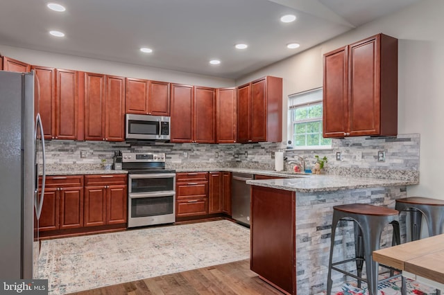 kitchen with stainless steel appliances, wood finished floors, a peninsula, decorative backsplash, and recessed lighting