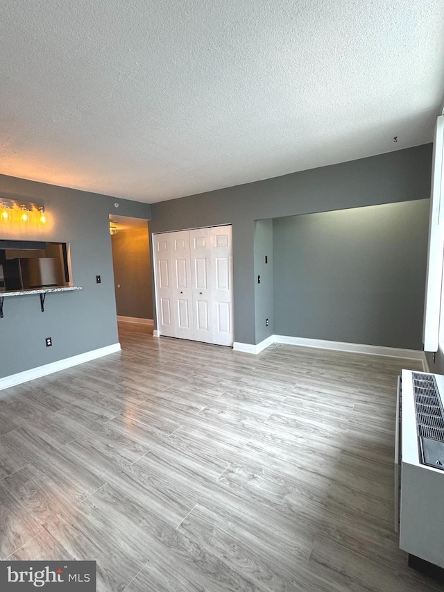 unfurnished living room with a textured ceiling, baseboards, and wood finished floors