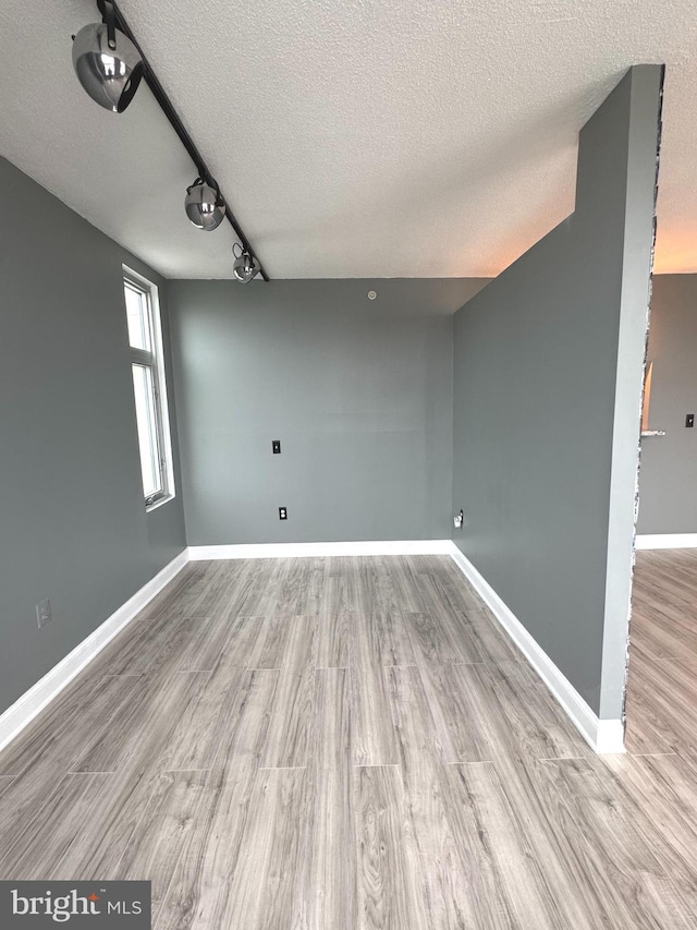 empty room with a textured ceiling, wood finished floors, baseboards, and track lighting