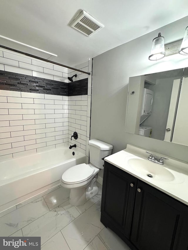 bathroom featuring stacked washer and clothes dryer, marble look tile flooring, toilet, bathing tub / shower combination, and vanity
