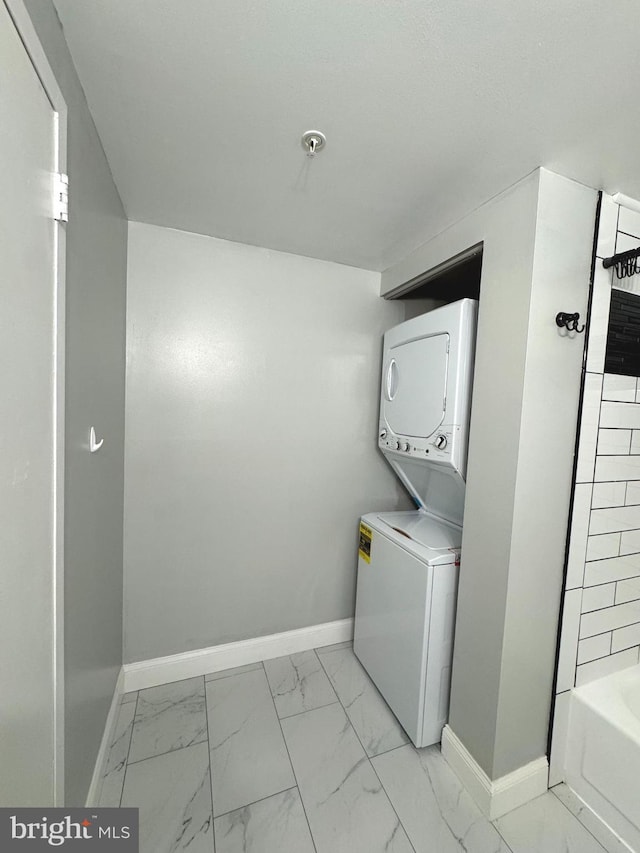 clothes washing area with stacked washer and clothes dryer, baseboards, and light marble finish flooring