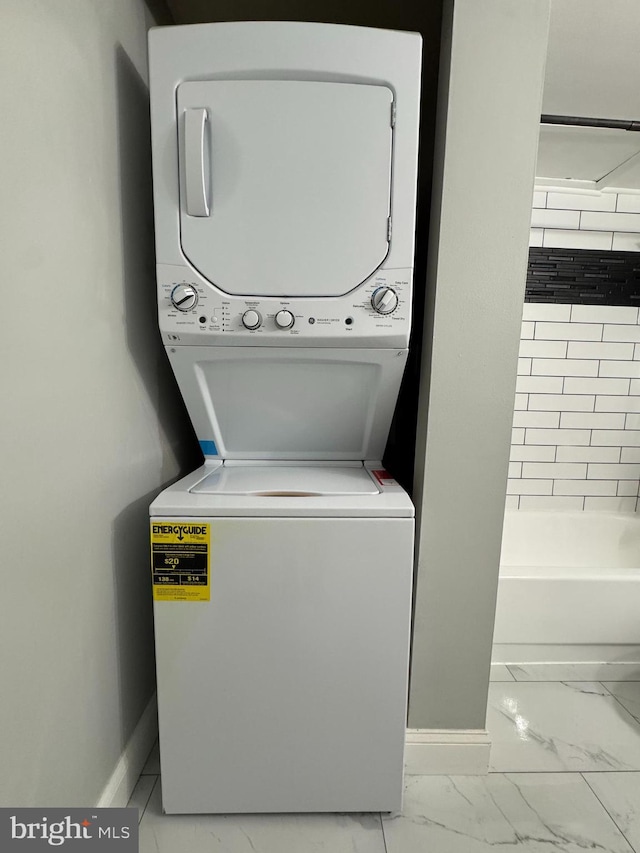 washroom with stacked washer / drying machine, marble look tile flooring, and baseboards