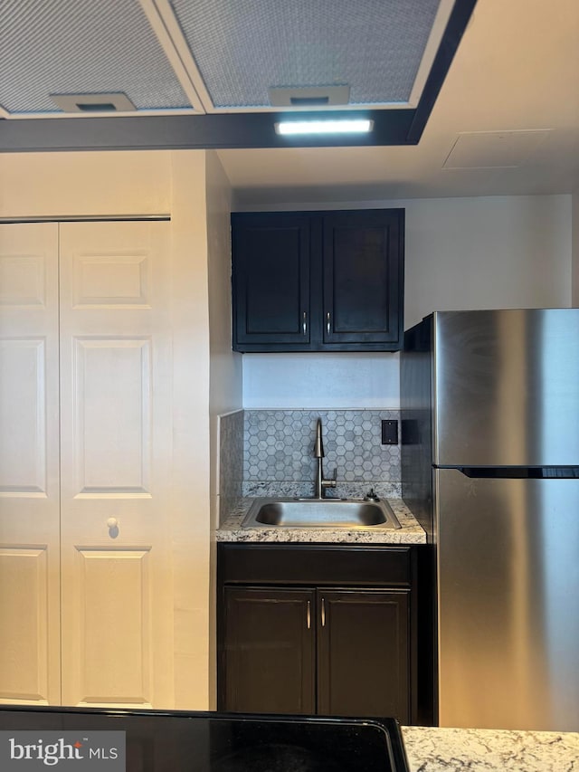 kitchen featuring freestanding refrigerator, a sink, backsplash, and light stone countertops