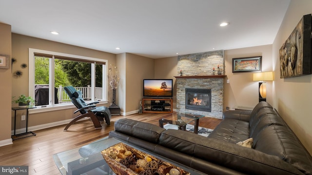 living room featuring a stone fireplace, wood finished floors, recessed lighting, and baseboards