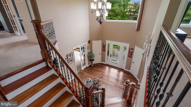 entryway featuring plenty of natural light, a chandelier, stairs, a towering ceiling, and wood finished floors