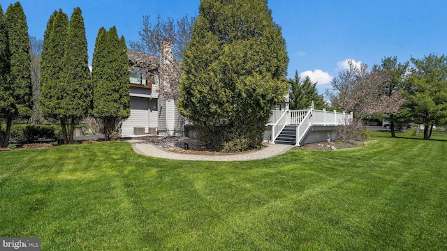 view of green lawn featuring a wooden deck and stairway