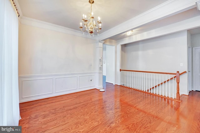 empty room with ornamental molding, a chandelier, wood finished floors, wainscoting, and ornate columns