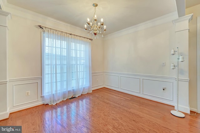 unfurnished room with a decorative wall, a chandelier, crown molding, wood finished floors, and wainscoting