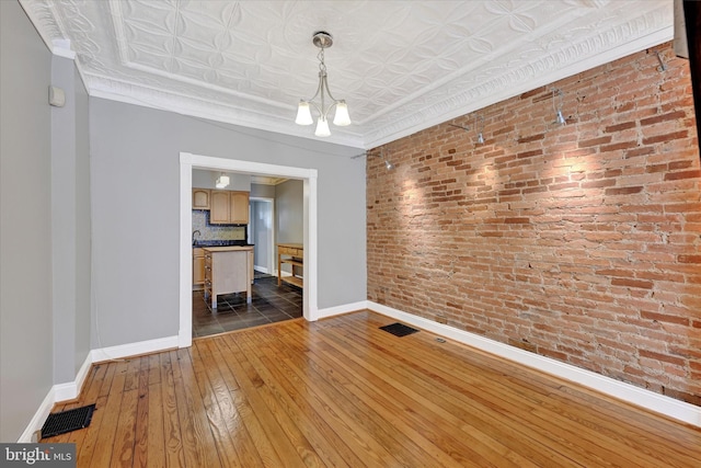 1407 Clarkson St, Baltimore, MD 21230 - unfurnished living room featuring brick wall, hardwood / wood-style flooring, baseboards, an ornate ceiling, and crown molding