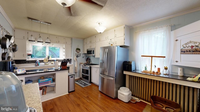 504 SE Front St, Milford, DE 19963 - kitchen with appliances with stainless steel finishes, radiator heating unit, wood finished floors, ornamental molding, and white cabinets