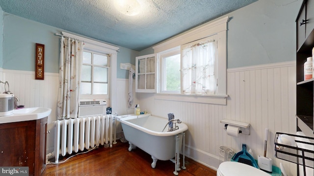 504 SE Front St, Milford, DE 19963 - bathroom featuring radiator, wainscoting, a freestanding bath, a textured ceiling, and wood finished floors