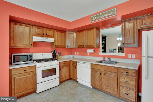 kitchen with white appliances, a sink, under cabinet range hood, and light countertops