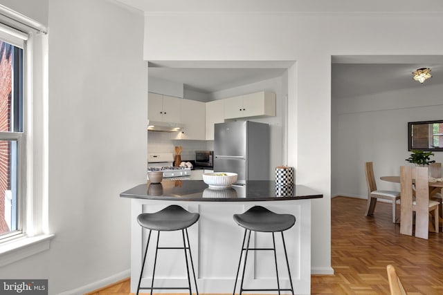 kitchen featuring appliances with stainless steel finishes, under cabinet range hood, dark countertops, backsplash, and a peninsula