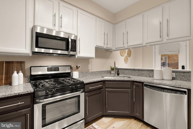 kitchen featuring stainless steel appliances, a sink, white cabinets, light stone countertops, and light wood-style floors