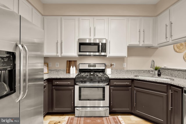 kitchen featuring appliances with stainless steel finishes, a sink, white cabinets, and light stone counters
