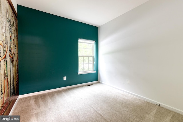 carpeted spare room featuring baseboards and an accent wall